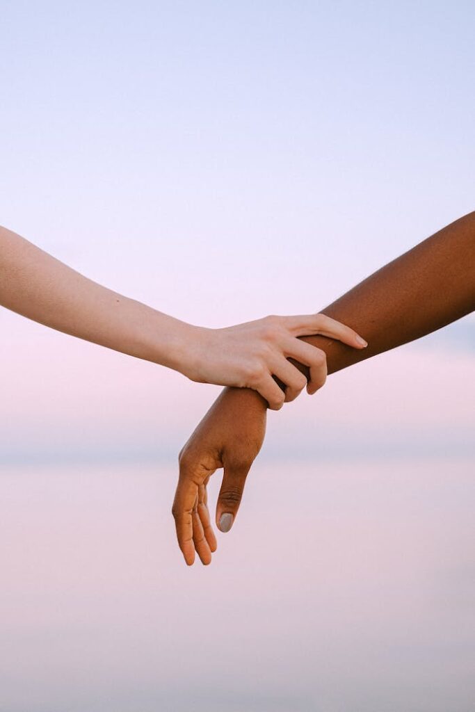pexels-photo-4672710 Close-up of two different skin toned hands holding gently against a serene sunset sky.